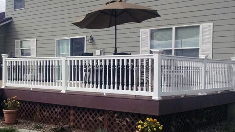 Durables Ashington t-top vinyl rail with colonial-style balusters and Federation Post Caps is installed on a dark brown deck outside of a gray house