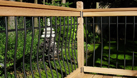 Vista's curved metal baluster with wood rail kit is installed on a wood deck on a wooded backyard during mid-day.