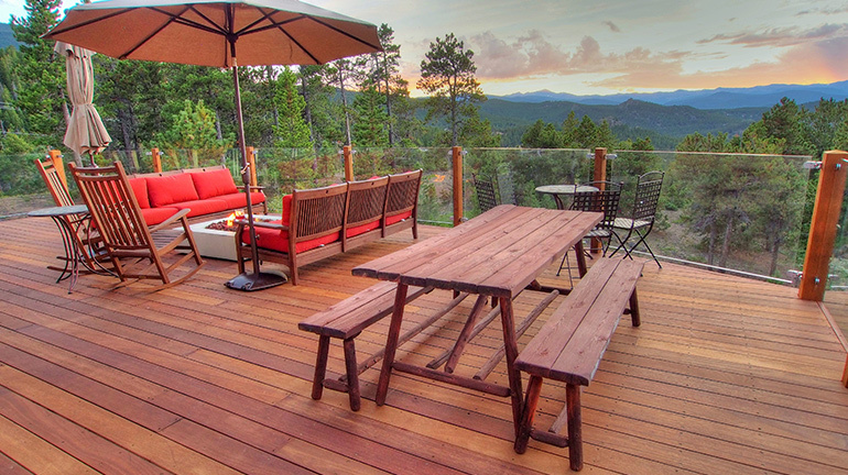 A hardwood deck decorated with furniture and potted ferns is protected with Penofin Penetrating Oil.