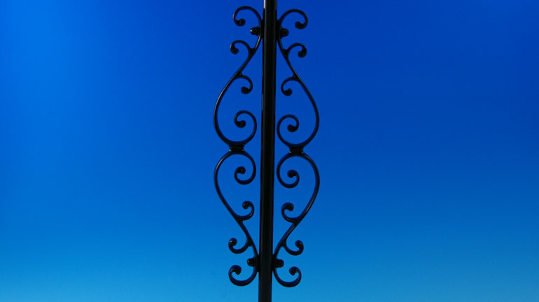 Black Classical Centerpiece by Deckorators installed on a black baluster in front of a blue background.