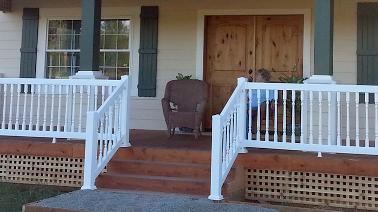 Durables premium Westport vinyl railing with standard top rail and colonial style balusters is installed on a front porch and stairway, featuring 4