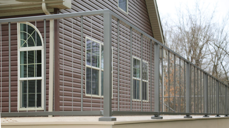 Westbury VertiCable with Crossover Posts is installed on a light brown composite deck in front of a brown house