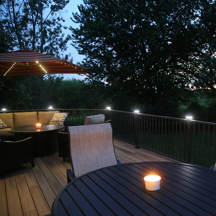A night view of lounge furniture on a deck illuminated by a candle and post cap lights from Magena Star Lighting by Westbury