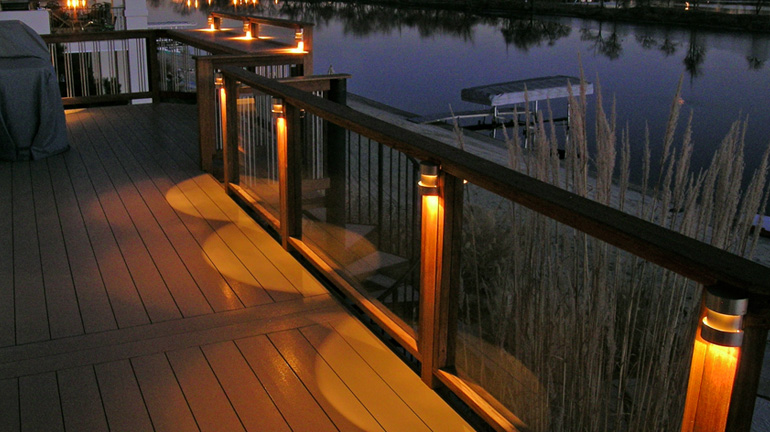 A waterfront deck railing is illuminated with a Highpoint Berkley LED Rail Lights at each post