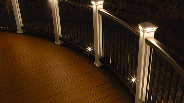 Curved Trex Transcend Railing is illuminated by LED Pyramid Post Cap Lights and the perimeter of the deck is outlined with Recessed LED Dot Deck Lights from Trex DeckLighting