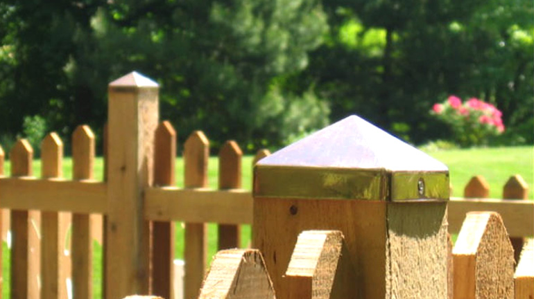 Cedar picket fence has posts topped with pyramid Copper Post Caps