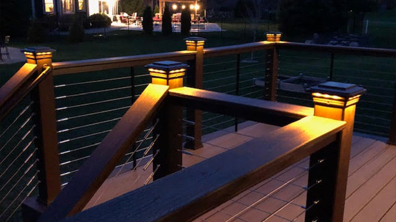 A decorative vinyl front porch railing with colonial-style balusters is highlighted with white aluminum solar post cap lights and Solar Deck Lighting from Classy Caps