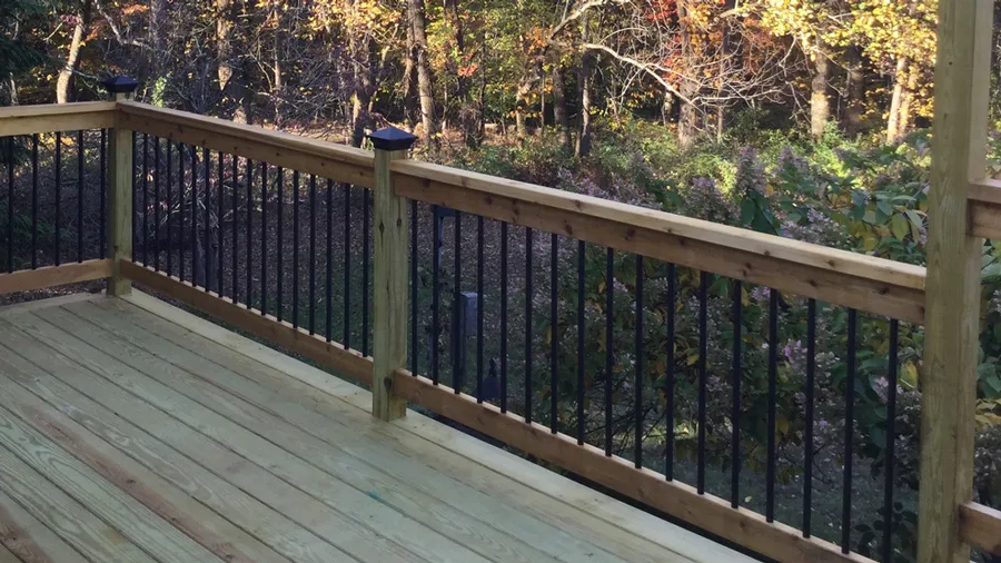 A wood deck railing with metal balusters and post caps
