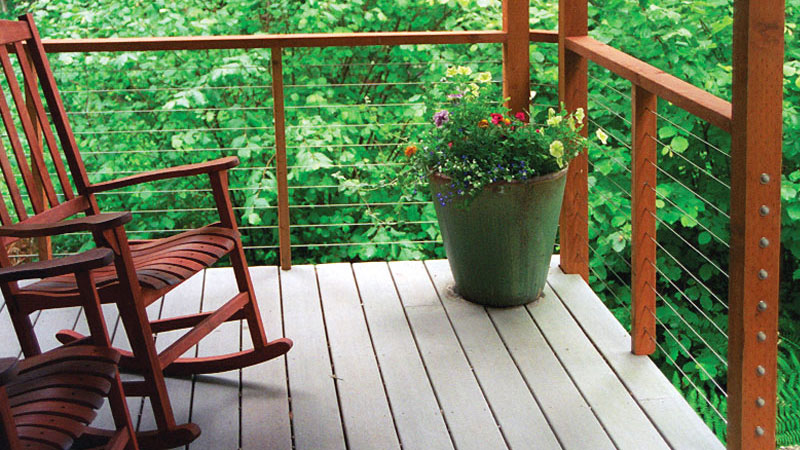 A cedar wood deck railing with Feeney cable runs between the posts