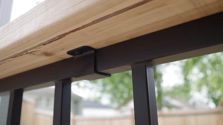 Cap rail clips attach a wood deck board to the top of a metal railing as a functional drink rail