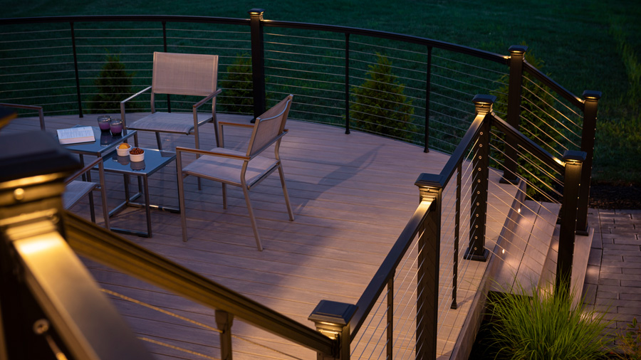 A deck featuring Key-Link cable railing and beautiful lit post caps at night