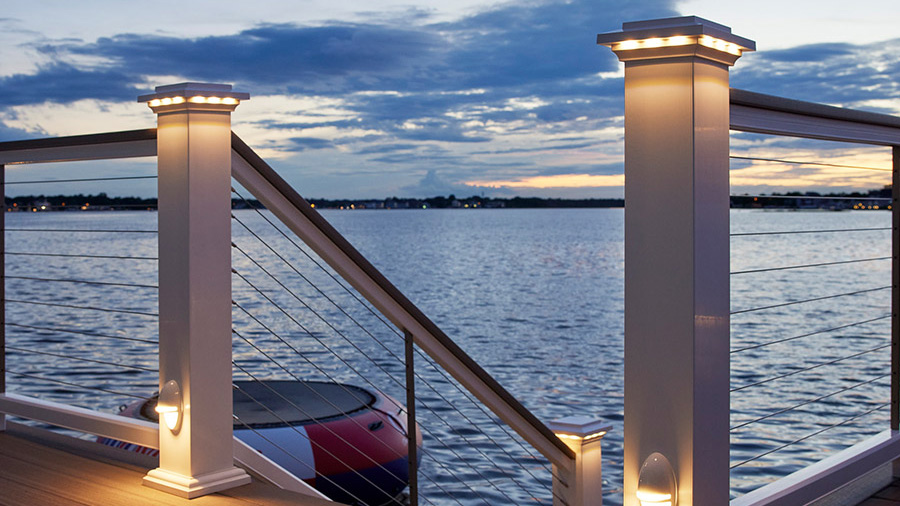 A classic, traditional deck railing lit up at night by a lake